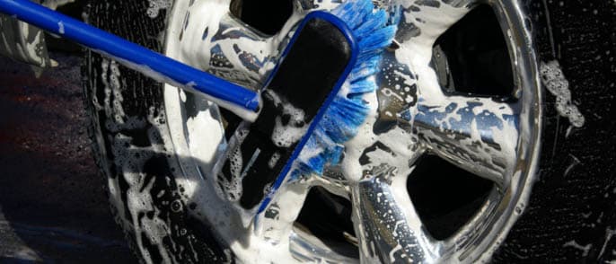 Using a blue tire brush to clean a tire and wheel with soap and water
